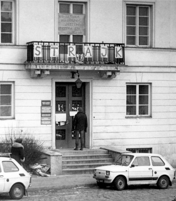 czarno-białe zdjęcie wejścia do budynku z napisem strajk